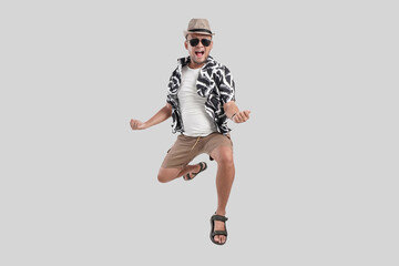 Wall Mural - Excited happy young Asian man tourist wearing sunglasses jumping over isolated white background.