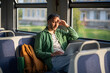 © DimaBerlin - Thoughtful tired man works on laptop in train car, shading eyes from bright sunlight. Remote work, digital nomad, work commute, travel work portability, productivity on move, work life balance