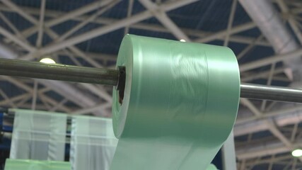 Poster - A roll of plastic wrap is hanging from a metal rod. The plastic wrap is green and he is a type of plastic wrap used for food