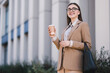 © New Africa - Smiling businesswoman in stylish suit with paper cup outdoors, low angle view. Space for text