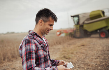 Wall Mural - Farmer with tablet in front of combine harvester in field