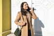 © Srdjan - Attractive brunette businesswoman talking on mobile phone with client. Business female office worker discussing on smart phone with employer, outdoor on the street.