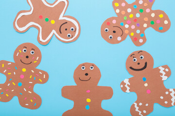Wall Mural - Brown gingerbread man shapes with colorful pattern from application paper on light blue table background. Pastel color. Making and creating decoration elements. Closeup. Top down view.