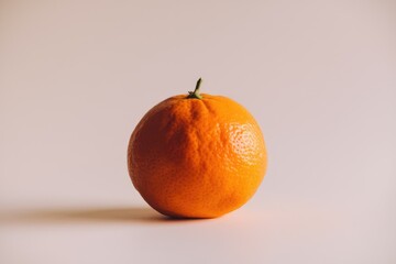 Poster - A single, ripe orange sits on a plain background, showcasing its vibrant color and texture.