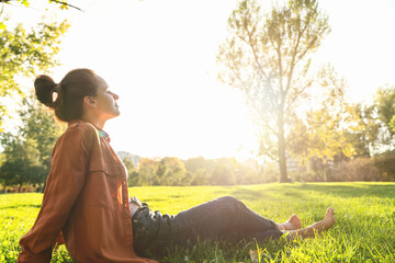 Urban woman sitting on the green grass in city park relaxing after work. Work and life balance, mental health and recovery.