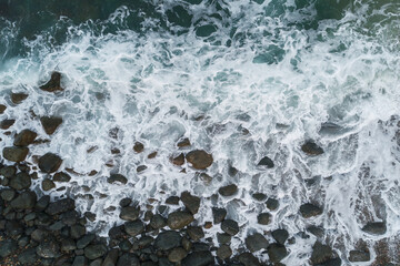 Poster - A rocky shoreline with a large wave crashing against the rocks. The water is white and frothy, and the rocks are scattered throughout the scene. Scene is one of power and strength