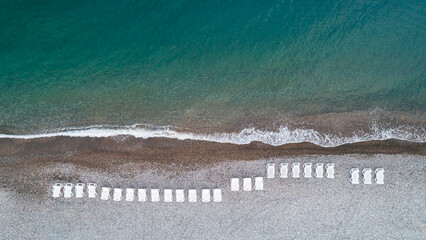 Poster - A beach with a row of white beach chairs. The chairs are lined up in a row, and the beach is calm and peaceful