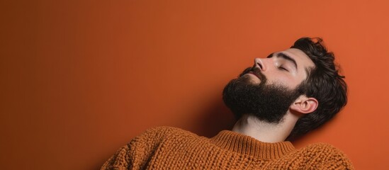 Poster - bearded young man in cozy brown sweater relaxing against vibrant orange wall with large empty space 