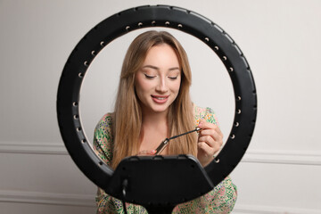 Canvas Print - Beautiful young woman with mascara for eyelashes near white wall, view through ring lamp