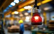 © nitnicha - A red work lamp hangs in an industrial setting, illuminating the workspace with a soft glow while a worker is blurred in the background.