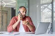 © Liubomir - Serious focused man talking on the phone while sitting at a desk inside an office with a notebook, office worker businessman in a casual shirt.