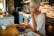 © Marko Geber - Senior woman working on laptop at modern kitchen