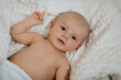 © Vasil - A baby is laying on a white blanket with its eyes closed. The baby is smiling and he is content