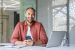 © Liubomir - Portrait of a young businessman with a phone in his hands, a man works inside an office at a workplace with a laptop, looking joyfully at the camera. Office worker in casual clothes.