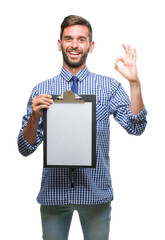 Wall Mural - Young handsome business man holding clipboard over isolated background doing ok sign with fingers, excellent symbol