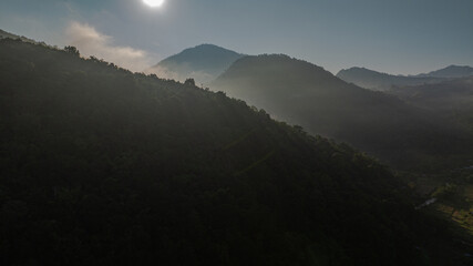 Wall Mural -  Aerial view of the sun above The sun over the mountain peaks shines through the valley. Cloudy skies and surrounding hills enhance the peaceful ambiance of this scenic setting.