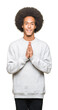 © Krakenimages.com - Young african american man with afro hair wearing sporty sweatshirt praying with hands together asking for forgiveness smiling confident.