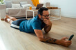 © simona - Man in his 50s lying on the floor in his apartment, using a phone to follow an online workout tutorial, performing fitness exercises to maintain his physical health and overall well-being at home