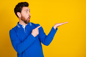 Poster - Photo portrait of attractive young man point hold empty space dressed stylish blue clothes isolated on yellow color background
