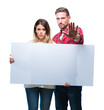 © Krakenimages.com - Young couple together holding blank banner over isolated background with open hand doing stop sign with serious and confident expression, defense gesture