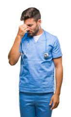 Wall Mural - Young handsome doctor surgeon man over isolated background tired rubbing nose and eyes feeling fatigue and headache. Stress and frustration concept.