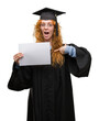 © Krakenimages.com - Young redhead woman wearing graduate uniform holding degree with surprise face pointing finger to himself