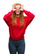© Krakenimages.com - Young redhead woman wearing red sweater doing ok gesture like binoculars sticking tongue out, eyes looking through fingers. Crazy expression.