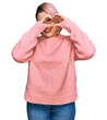 © Krakenimages.com - Hispanic woman with pink hair wearing casual winter sweater doing heart shape with hand and fingers smiling looking through sign