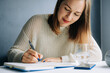 © Olga Moreira/Stocksy - Smiling woman holding pen while journaling at table with water a