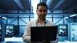 © DC Studio - System administrator in data center using notebook to design, implement and manage gear, ensuring optimal performance and reliability. Indian man in server room coding on laptop, camera B