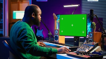 Leinwandbilder - Songwriter operates on synthesizer piano keys next to isolated display, composing new music with instruments and stereo tools in home studio. Artist producer works with green screen. Camera B.