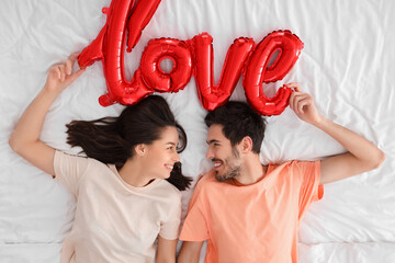 Canvas Print - Happy young couple with word LOVE made of balloons lying in bedroom on Valentine's Day, top view