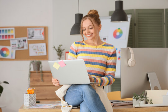 Female web designer with laptop sitting on table in office