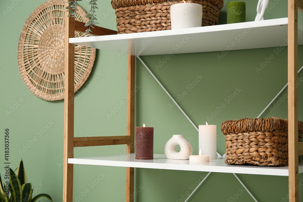 Burning candles on shelf near green wall in room