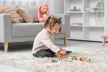 Wall Mural - Cute little girl with cubes learning alphabet on carpet at home