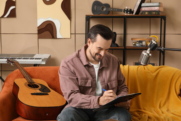 Wall Mural - Young happy male composer with guitar writing notes in music studio