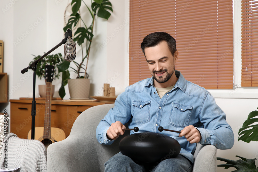 Young happy male composer with sticks playing glucophone on armchair at home