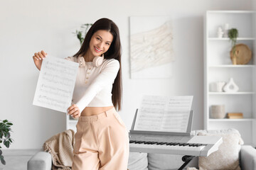 Wall Mural - Young woman with note sheet and synthesizer at home