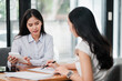 © Satori Studio - Two women engaged in a business meeting, reviewing documents and using a tablet in a contemporary office environment.
