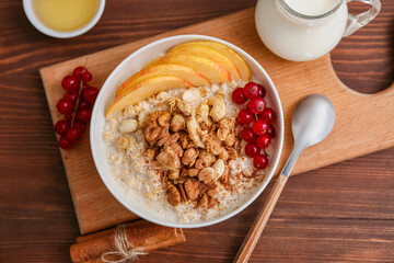 Wall Mural - Bowl with tasty oatmeal with berries and slices of apple on wooden background