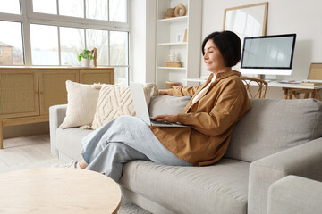 Sticker - Mature woman using laptop on sofa at home