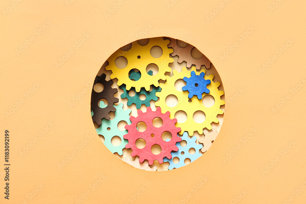 Wooden gears visible through round hole in orange paper