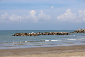 manmade rock formation island with gentle waves breaking on sandy shores under partly-cloudy skies