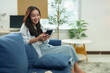 © Phimwilai - Young asian woman is using a smartphone and relaxing on a comfortable sofa in her modern living room, enjoying her leisure time and staying connected