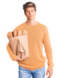 © Krakenimages.com - Young handsome man holding paper bag with bread thinking attitude and sober expression looking self confident