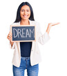 © Krakenimages.com - Young beautiful latin girl holding blackboard with dream word celebrating victory with happy smile and winner expression with raised hands