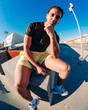 © Studio Marmellata - A young man in yellow shorts and white sneakers poses confidently on a concrete urban ledge captured under bright sunlight and a vivid blue sky using a fisheye lens perspective