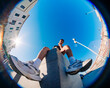 © Studio Marmellata - A low-angle fisheye view of a young man in athletic attire seated on a concrete ledge in an urban environment with clear skies and bright sunlight in the background.