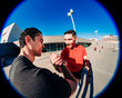 © Studio Marmellata - Two young men doing sport activity captured in a fisheye lens perspective, one wearing a red shirt and the other in black, engaging in a handshake under a sunny blue sky