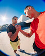 © Studio Marmellata - Two young men doing sport activity captured in a fisheye lens perspective, one wearing a red shirt and the other in black, engaging in a handshake under a sunny blue sky